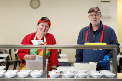 Two people preparing food in our Dining Hall and smiling into the camera